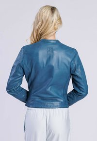 Veste en cuir pour femmes de couleur bleue, avec un col rond, un design ajusté et un petit patch logo dans le dos. Texture lisse et matériel minimal.