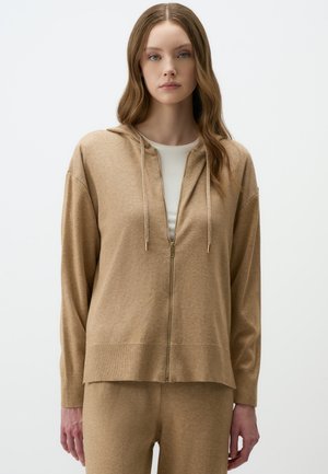 Beige zip-up hoodie with a hood, featuring a lightweight texture, front zipper, and ribbed cuffs. Paired with matching beige pants.