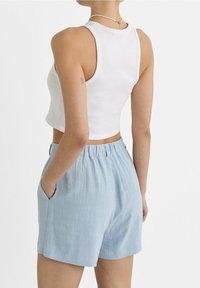 Top corto bianco abbinato a pantaloni corti blu chiaro, texturizzati, con cinturino elastico e tasche laterali.