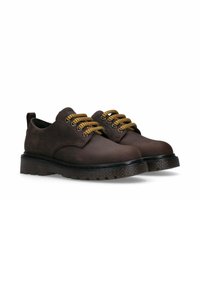 Bruine leren schoenen met een gestructureerd oppervlak, ronde neus en dikke zwarte zool. Voorzien van gouden veter met standaard oogjes en een trekband aan de achterkant.