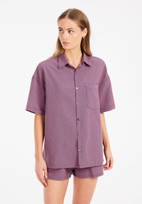 Camicetta a maniche corte con bottoni, in un motivo a quadri viola e rosso, dotata di tasca e vestibilità rilassata, abbinata a pantaloni corti coordinati.