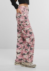 Pantalone cargo u kamuflažnom uzorku u ružičastoj, crnoj i krem boji, opuštenog kroja, s više džepova i čvrstim pojasom. Teksturirana tkanina, izblijedjeli dizajn.