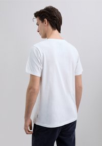 Maglietta bianca di cotone con scollo rotondo e maniche corte, con una texture liscia e una vestibilità comoda. Nessun logo o motivo visibile.