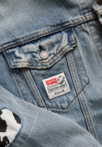 Gaiši zils džinsu jaciņa ar priekšējo kabatu, sudraba pogu, kā arī birkām, uz kurām rakstīts "Levi's Authentic Western Wear" un "Pixar". Izšķirīga pazīme ir melnbalta govs druka.