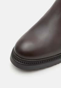 Stivale alla caviglia in pelle marrone con punta arrotondata, suola in gomma texture e dettagli cuciti lungo il bordo della suola per una maggiore aderenza.