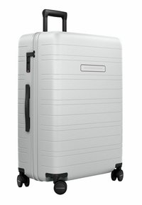 Valise rigide blanche avec un design rainuré, poignée noire rétractable, accents noirs et quatre roulettes pour la mobilité.