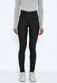 Högmidjade svarta jeans med en slät textur, femficksdesign och slim fit, i kombination med vita sneakers och en grå långärmad topp.