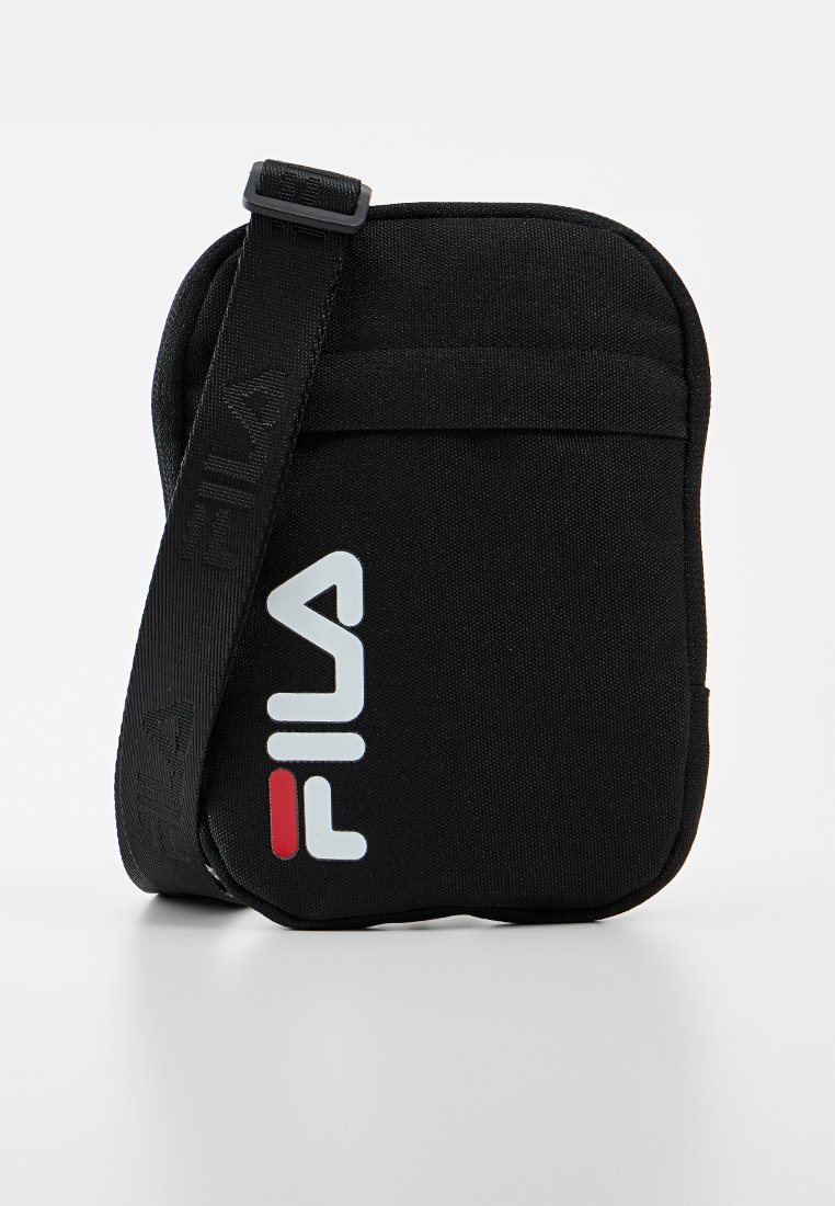 Svart kompakt crossbody-väska med justerbar axelrem och en djärv FILA-logotyp i vitt och rött på framlappen.