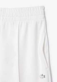 Pantaloni de trening albi cu talie elastică, buzunare laterale și un mic logo brodat pe piciorul inferior. Material neted, cu textură.