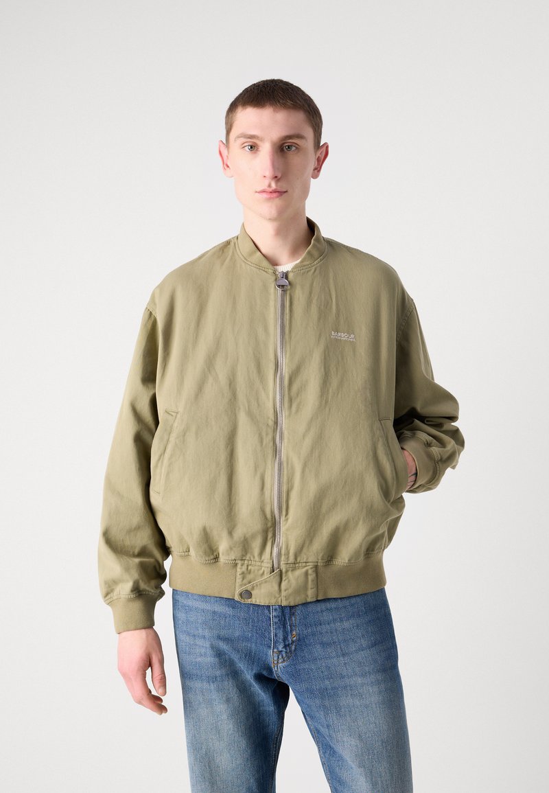Olivegrüner Bomberjacke mit Reißverschlussfront, gerippten Bündchen und Saum sowie seitlichen Taschen. Verfügt über ein kleines Logo auf der Brust. Kombiniert mit blauen Jeans.