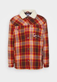 Koszula flanelowa w kratę w odcieniach pomarańczowym, czerwonym i brązowym. Posiada sztuczny kołnierz z owczej wełny, dwie przednie kieszenie oraz białe haftowane detale.