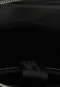 Interno di una borsa nera con texture liscia e un'etichetta intrecciata. Presenta una cerniera argentata lungo la parte superiore. L'ambiente è scuro.