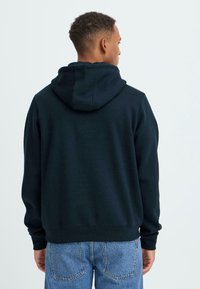 Svart hettegenser med romslig hette, ribbestrikkede mansjetter og kant, samt et mykt, teksturert stoff. Brukt med lyseblå, løse jeans.