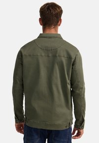 Olivgrüne Jacke mit strukturiertem Kragen, knöpfbaren Bündchen und leicht geschwungenem Saum. Hergestellt aus robustem Stoff mit sichtbaren Nähdetails.