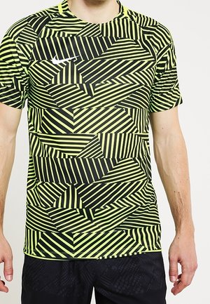 Mężczyzna noszący sportową koszulkę z krótkim rękawem z neonowożółtym i czarnym geometrycznym wzorem pasków oraz małym białym logo Nike na piersi.