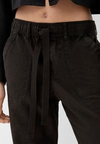 Pantalon à taille élastique noire avec une fermeture par lien en tissu, doté de deux poches latérales et d'une finition lisse et texturée.