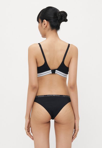 Black lingerie set featuring a sleek bralette with adjustable straps and a waistband detail. Smooth fabric with a minimalist design.