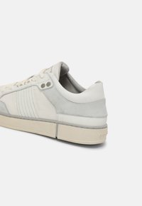 Helle graue Sneakers aus Leder und Wildleder, die kontrastierende Texturen, ein minimalistisches Design, flache Schnürsenkel und eine Gummisohle aufweisen.