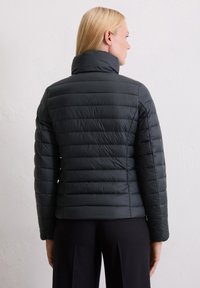 Polstret svart jakke med høy krage og horisontal quiltedesign. Glatt tekstur med en tettsittende silhuett som viser bakvurdering.