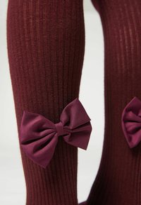 Bordeaux knäkorta strumpor med ribbad textur, som har stora satängrosetter i matchande färg på varje sida. Mjuk stickad kvalitet för komfort.