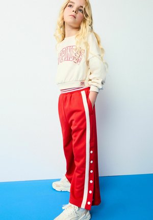 Røde sweatpants med hvide sidelommer og trykknapper, parret med en kremfarvet sweatshirt med teksten "HAPPINESS" i pink. Teksturstof.