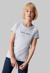Camiseta de algodón de color azul claro con mangas cortas y cuello redondo, con "Calvin Klein" bordado en gris oscuro a lo largo del pecho.