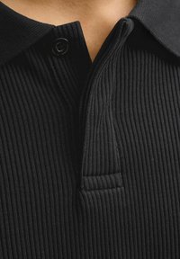 Gros plan d'un polo en maille côtelée noire avec un bouton fermé et un col retourné.