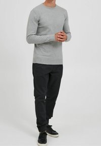 Pullover grigio a maniche lunghe con colletto rotondo, texture liscia e vestibilità slim; abbinato a pantaloni neri affusolati e sneaker nere.