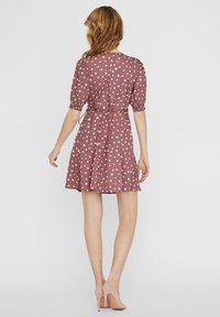 Kurzärmliges, gepunktetes Kleid in staubigem Rosa mit tailliertem Schnitt, schwingendem Rock und strukturiertem Stoff. Mit einem Bindeband am Rücken akzentuiert.