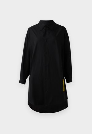 Camisa negra de manga larga hecha de una tela suave. Presenta un botón en la parte delantera, un cuello clásico y una etiqueta de acento amarilla en el lado.