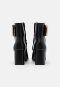 Černé kožené kotníkové boty na vysokém blokovém podpatku s výraznou zlatou sponou na boku, hladkým povrchem a elegantním stylem.