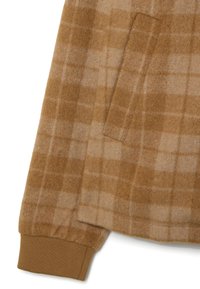 Tessuto in flanella quadrettata marrone con tasca laterale, polsino a costine in un marrone più scuro e tessitura morbida con finitura leggermente pelosa.