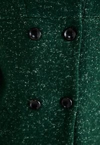 Manteau en mélange de laine vert avec une finition texturée, design double boutonnage et deux boutons noirs pour fermeture.