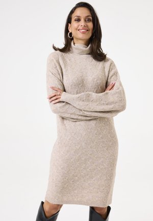 Beige gebreide coltrui jurk met een textuurpatroon, lange mouwen en een losse pasvorm, gecombineerd met hoge zwarte laarzen.