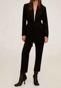 Sort skræddersyet blazer med bælte i taljen, to forlommer og matchende skræddersyede bukser. Sættet har slanke, spidse sorte ankelstøvler.