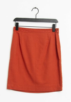 Jupe rouge, de longueur genoux, en tissu texturé, avec une taille ajustée et une fermeture éclair sur le côté. Accrochée à un cintre en plastique noir.