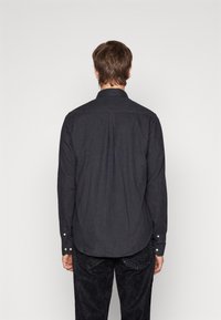 Camicia button-up grigia scura con colletto, maniche lunghe e due polsi con bottone, dotata di una piega sul retro per una maggiore libertà di movimento e una texture liscia.