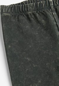 Svarta stretchbyxor med en strukturerad, sliten utseende. Funktioner en elastisk midja med rynkade detaljer. Mjuk, flexibel tyg.