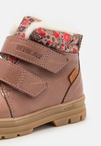 Brun læderstøvle med blomsterstoffor, grå manchette, to velcro-remme, gummisål og præget logo. Bemærk: blødt futtrim på toppen.