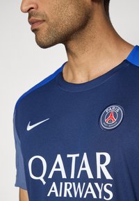 Mørkeblå Nike trøje med rund halsudskæring, blå detaljer på skuldrene og hvid "QATAR AIRWAYS" logo; har Paris Saint-Germain-logoet.