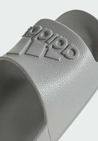 Šedé plastové sandály s texturovaným vrškem, s vyvýšeným logem a třemi pruhy. Otevřená špička a pohodlné nošení.