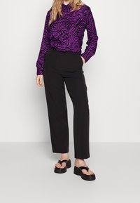 Blouse violette à manches longues avec un imprimé zèbre noir, associée à un pantalon noir à jambes droites et des sandales noires à semelles épaisses. Design simple, texture lisse.