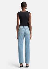 Top nero senza maniche abbinato a jeans a vita alta di un blu chiaro con gamba dritta. Si notano il corpetto aderente e i dettagli classici delle tasche in denim.