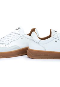 Sneaker bianche in pelle con dettagli perforati, suola in gomma marrone e accenti con logo. Texture liscia, design classico a basso profilo.