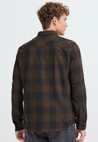 Camisa de cuadro marrón y negra, de manga larga, de suave tela tejida, con cuello, puños abotonados y dobladillo trasero recto.