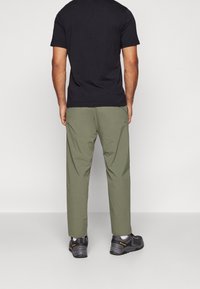 Herre sort t-shirt i kombination med olivenfarvede bukser. Outfitet har en afslappet pasform med blødt stof og sorte vandresko med grå detaljer.
