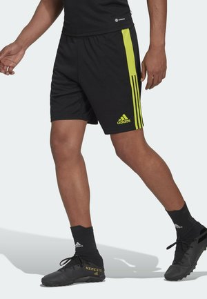 Gambe con pantaloncini Adidas neri con strisce e logo al neon, calzini Adidas neri e scarpe da calcio nere con marchio dorato "Nemeziz".