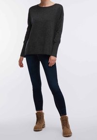 Grijze langwerpige trui met lange mouwen, ontspannen pasvorm, gecombineerd met donkerblauwe skinny jeans. Bruine veterschoenen tot de enkels met textuuraccenten.