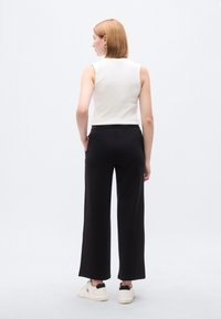 Λευκή μπλούζα χωρίς μανίκια με στρογγυλή λαιμόκοψη, συνδυασμένη με μαύρο παντελόνι φαρδύ και ψηλόμεσο. Παπούτσια λευκά αθλητικά με μαύρες λεπτομέρειες.