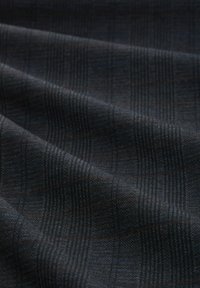 Textiel in donker marineblauw met een subtiel rasterpatroon, voorzien van verhoogde lijnen en fijne textuur. Draden in gedempt oranje versterken het ontwerp.